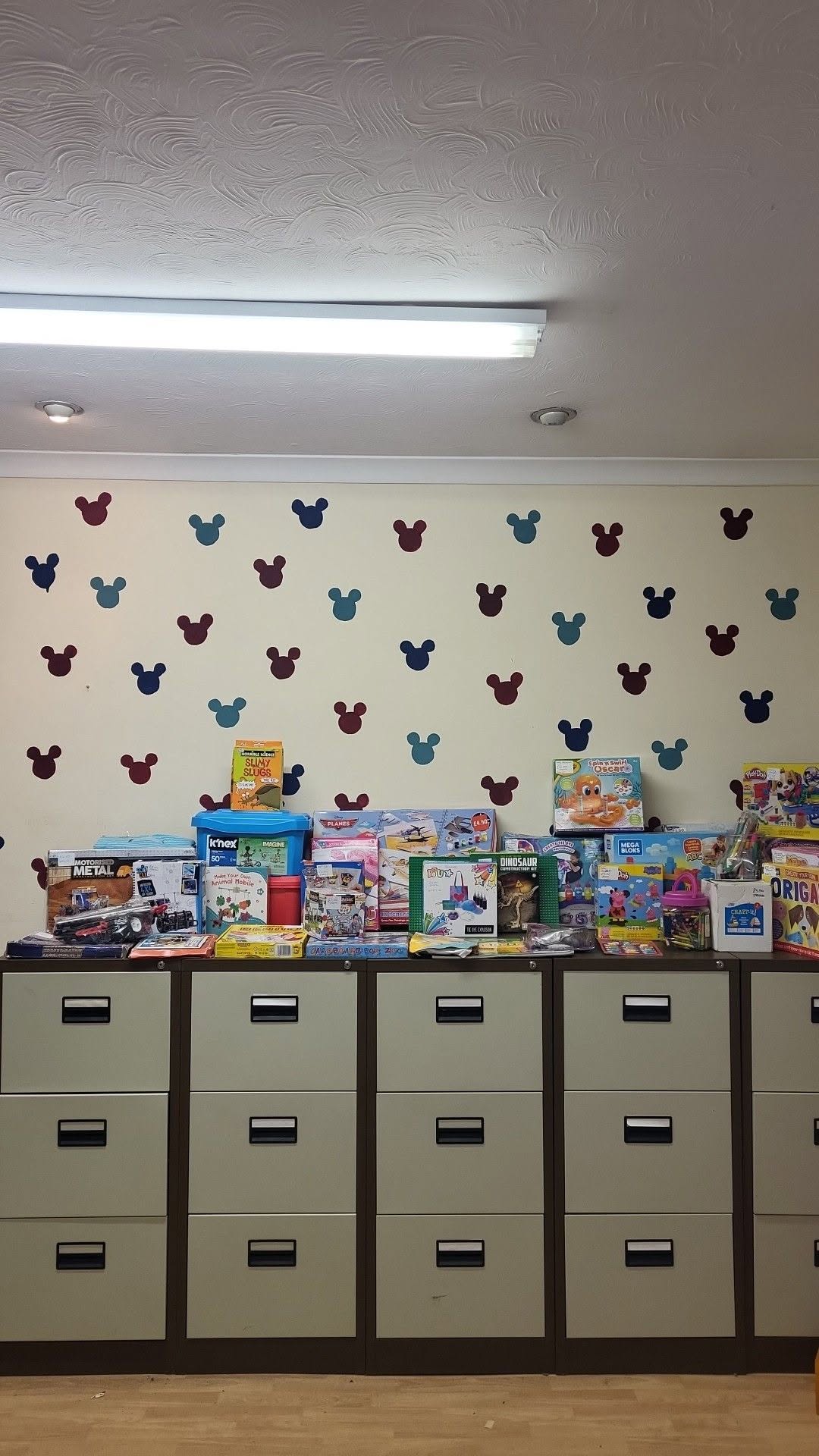 Her photograph of the room she calls Classroom 1 at Rogerstone: filing cabinets with boxed toys and craft kits on top, under a wall of Mickey Mouse shapes.